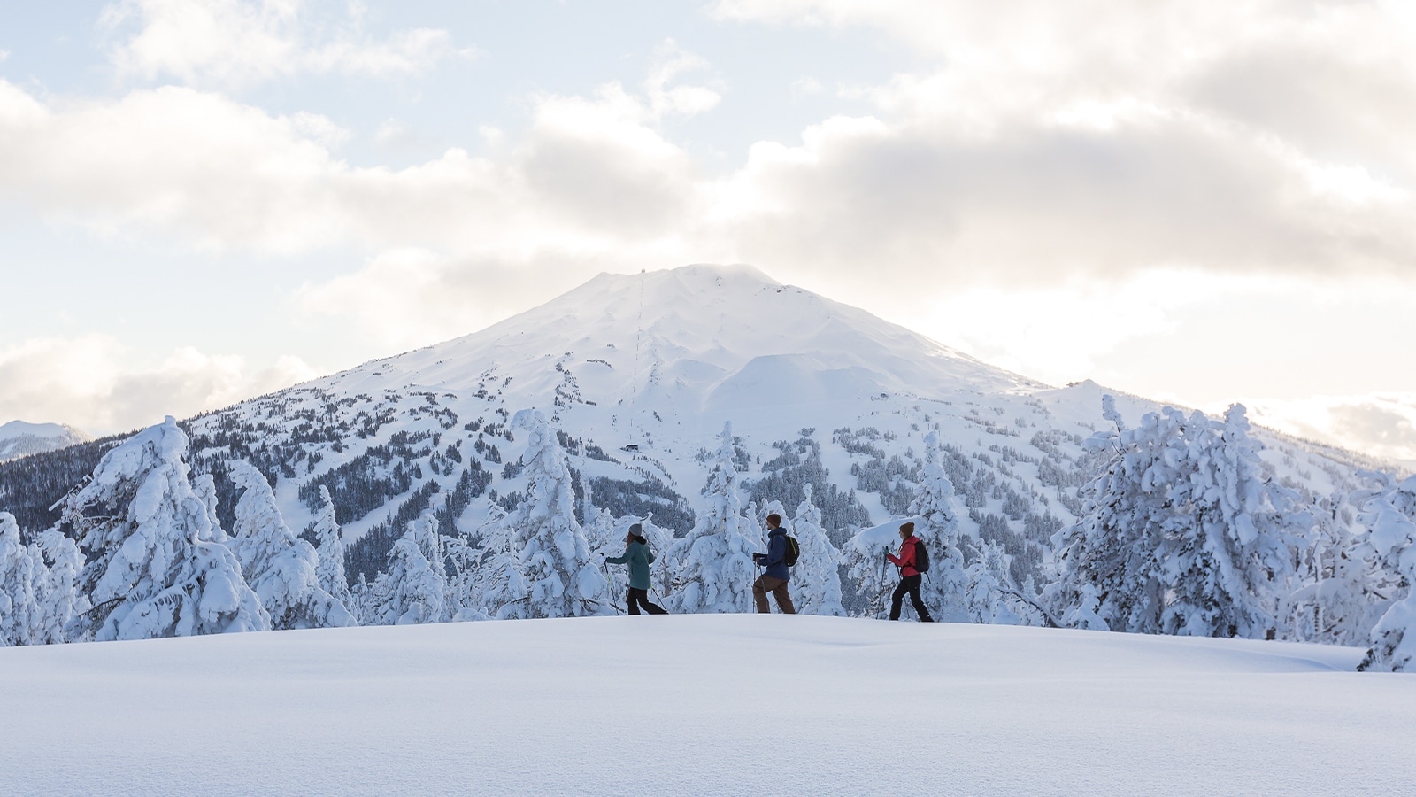 Three people snowshoe Tumalo Mountain near Bend, Oregon with a view of Mt. Bachelor behind them.